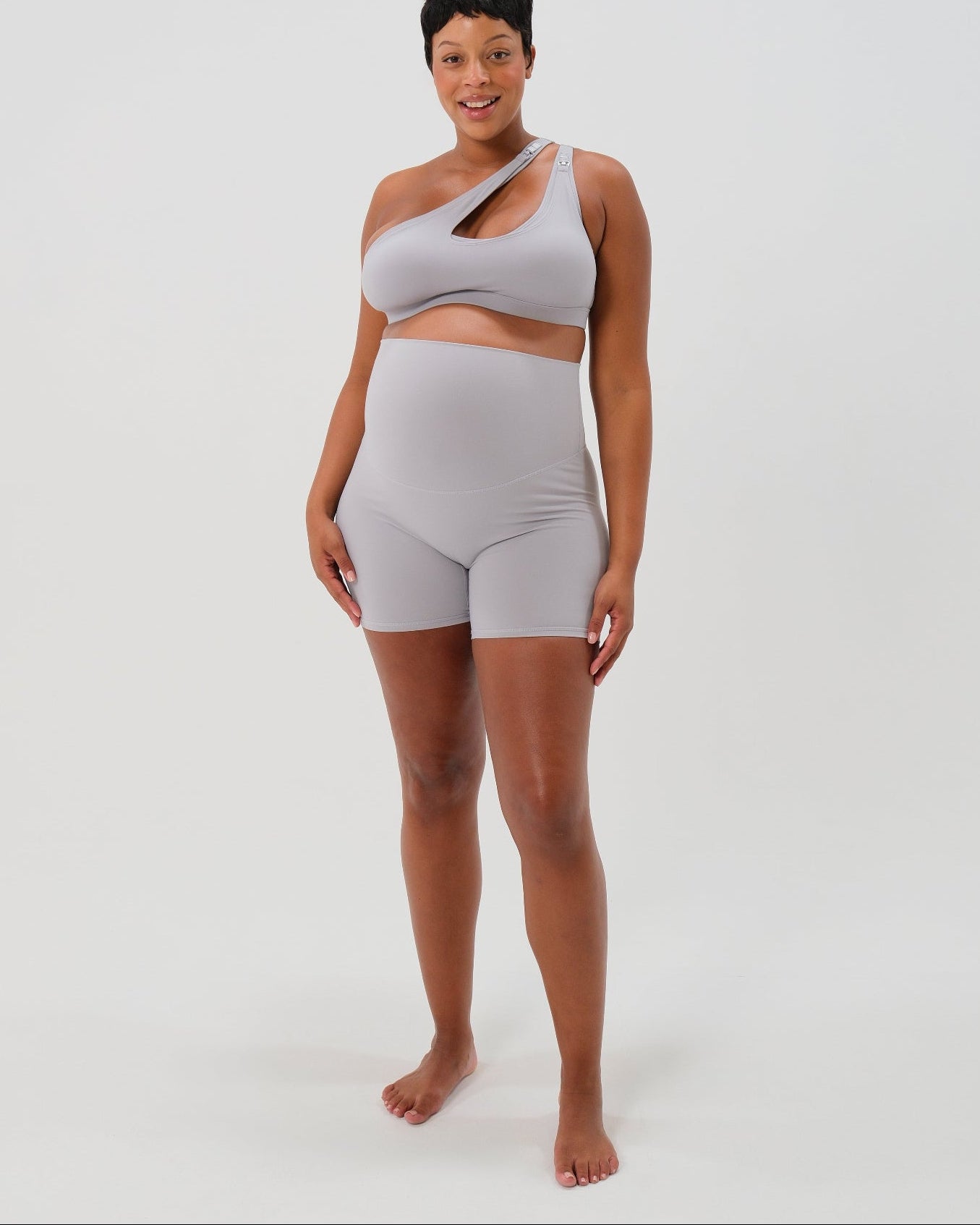 Pregnant plus size woman wearing premium light gray maternity bike shorts with a supportive high waist and matching high-impact, racerback maternity and nursing sports bra. Best reviewed 2026 premium maternity athletic and activewear by AXK, petite and tall friendly, in regular and plus size options.
