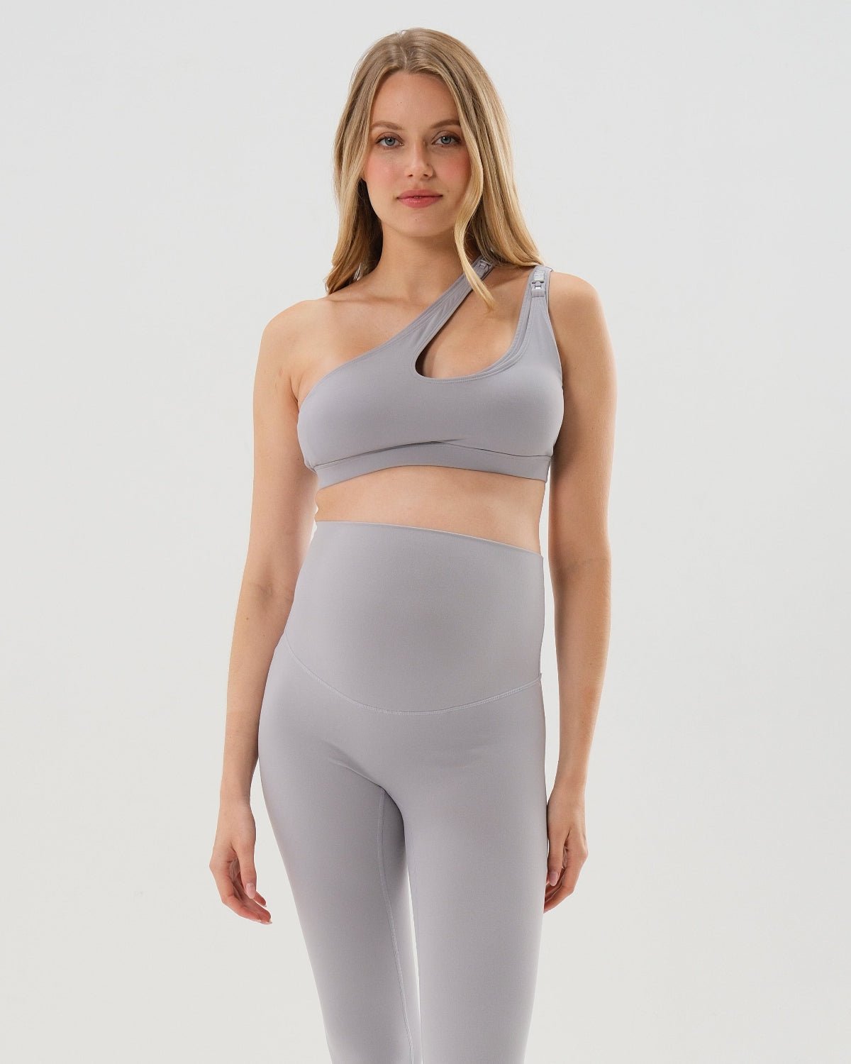 Light gray one-shoulder maternity and nursing sports bra and matching leggings. The bra features one-handed clip access for easy breastfeeding. Premium maternity activewear by AXK is offered in petite and plus size. 