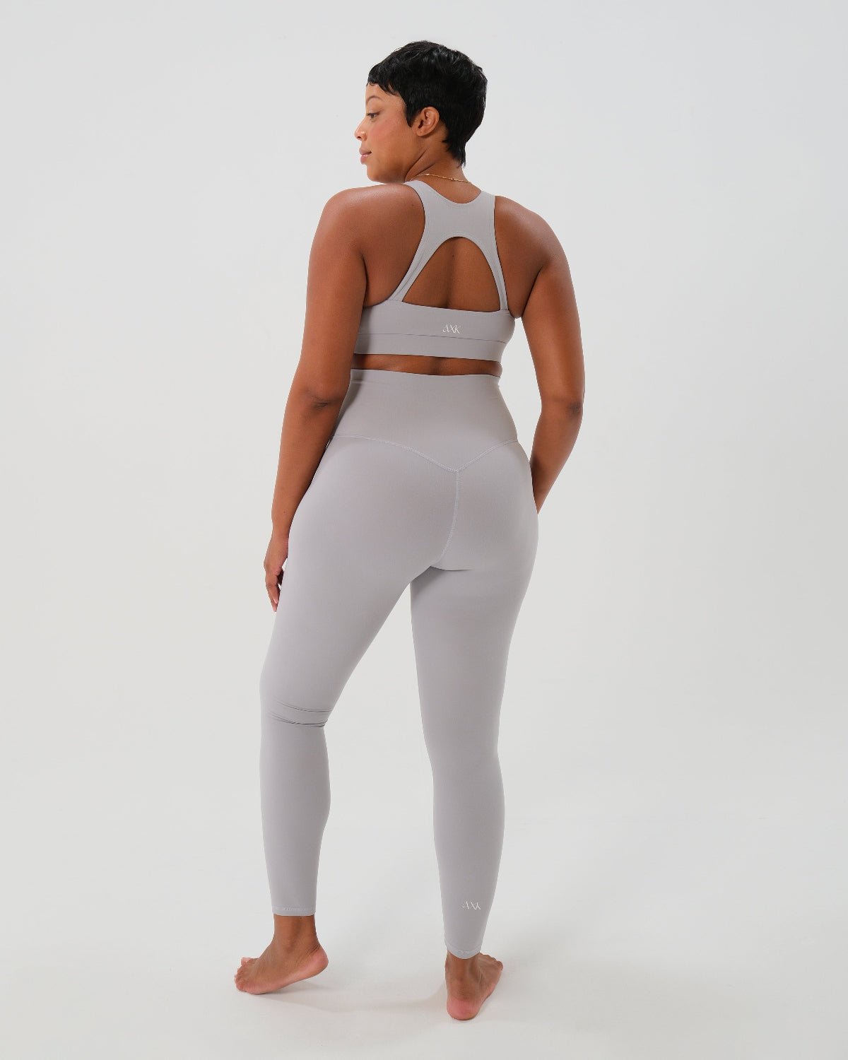 Light gray one-shoulder maternity and nursing sports bra and matching leggings. The bra features one-handed clip access for easy breastfeeding. Premium maternity activewear by AXK is offered in petite and plus size. Back view. 