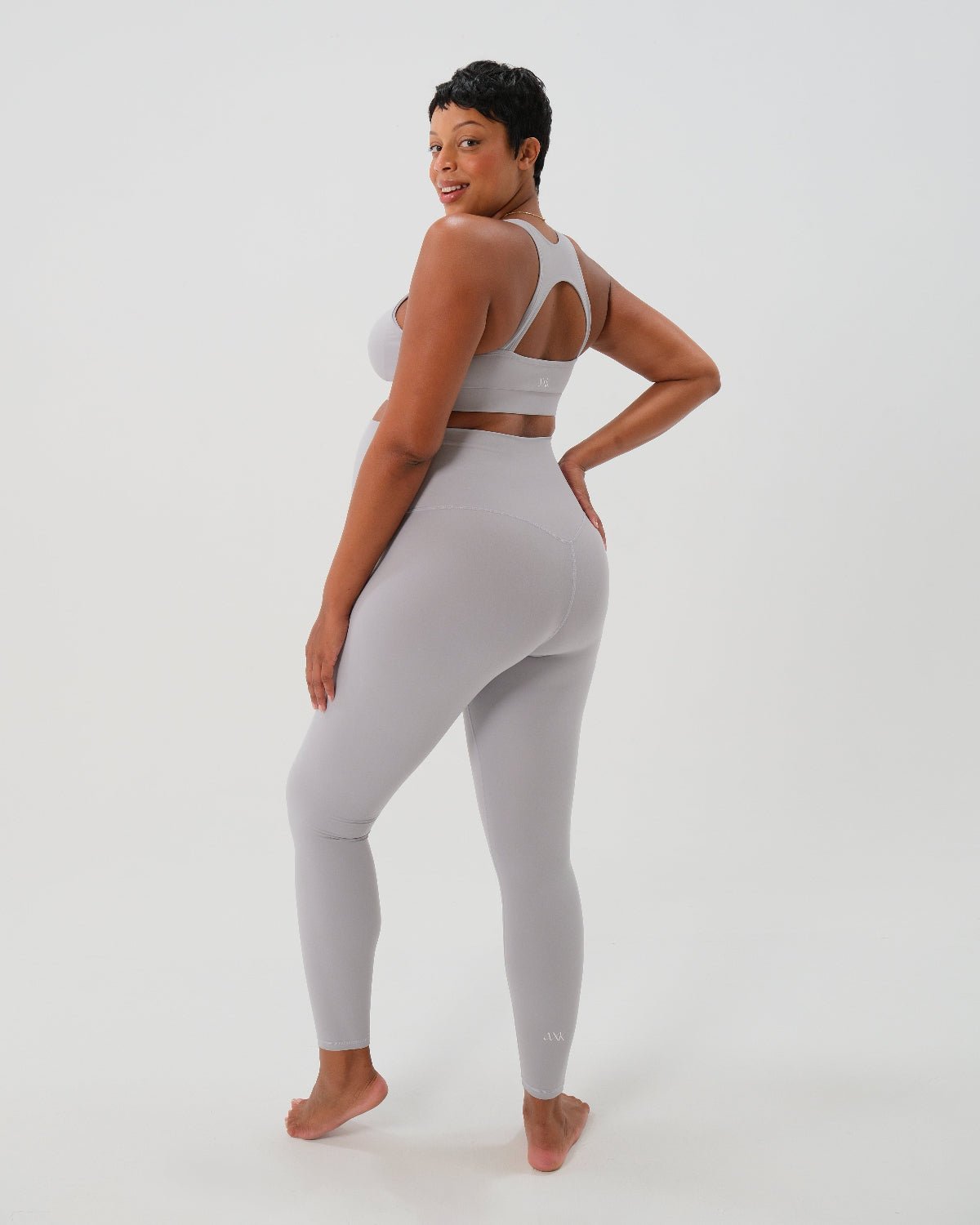 Pregnant woman wearing premium light grey maternity leggings with a flattering scrunch butt and supportive high waist and a high impact, racer back nursing sports bra on a white background. Premium maternity athletic and activewear by AXK - petite, tall and plus size friendly. 