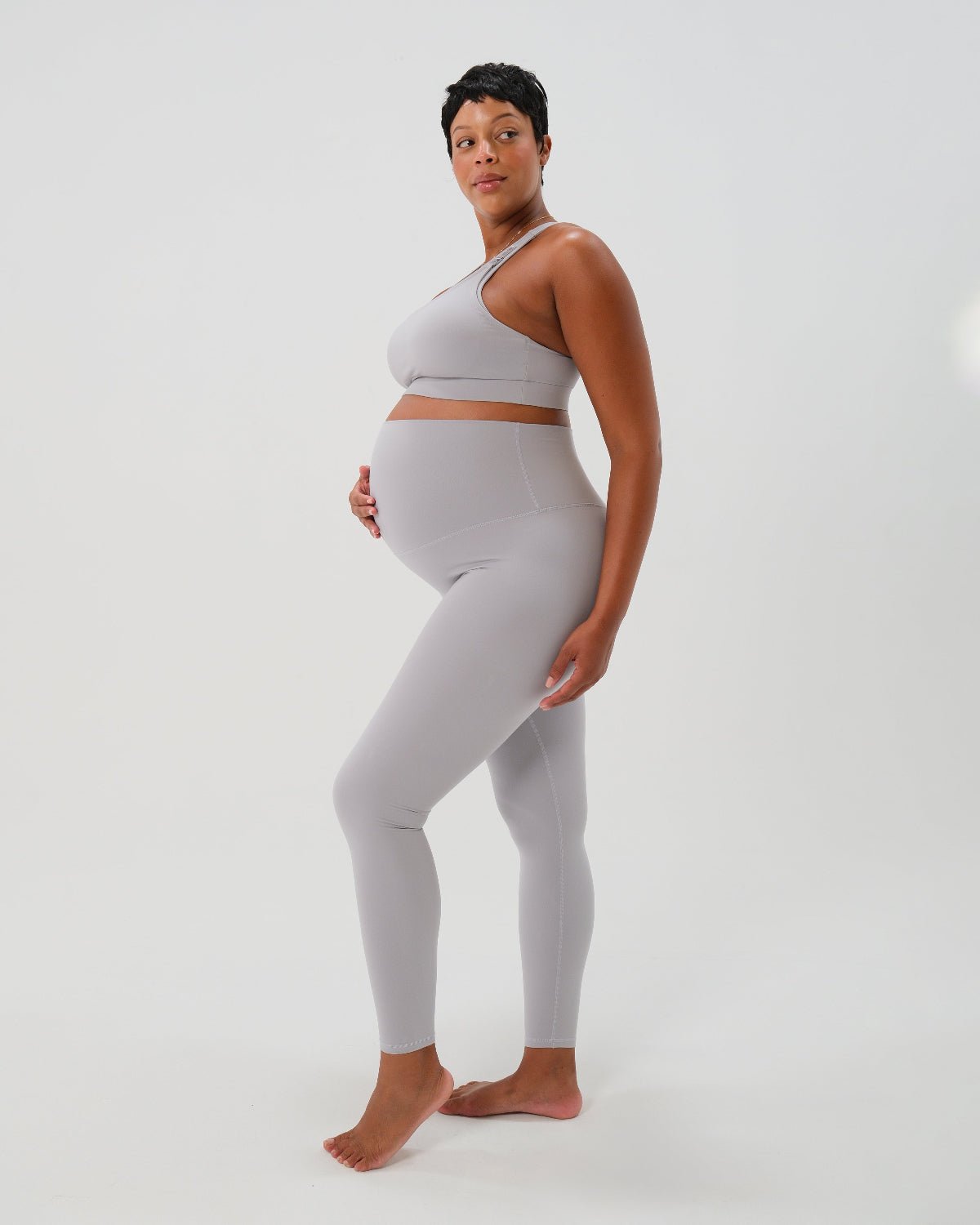 Pregnant woman wearing premium light grey maternity leggings with a flattering scrunch butt and supportive high waist and a high impact, racer back nursing sports bra on a white background. Premium maternity athletic and activewear by AXK - petite, tall and plus size friendly. 
