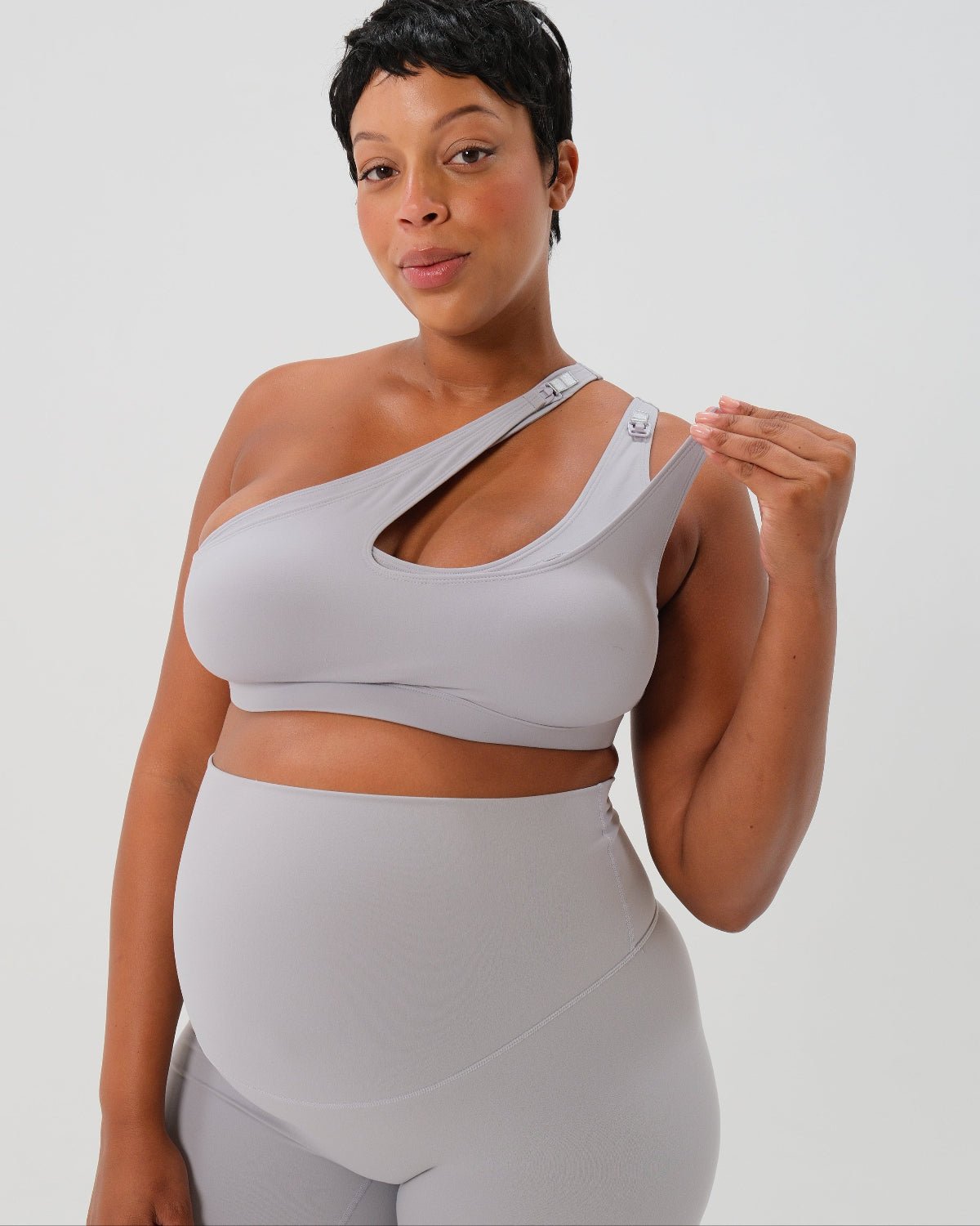 Light gray one-shoulder maternity and nursing sports bra and matching leggings. The bra features one-handed clip access for easy breastfeeding. Premium maternity activewear by AXK is offered in petite and plus size. 