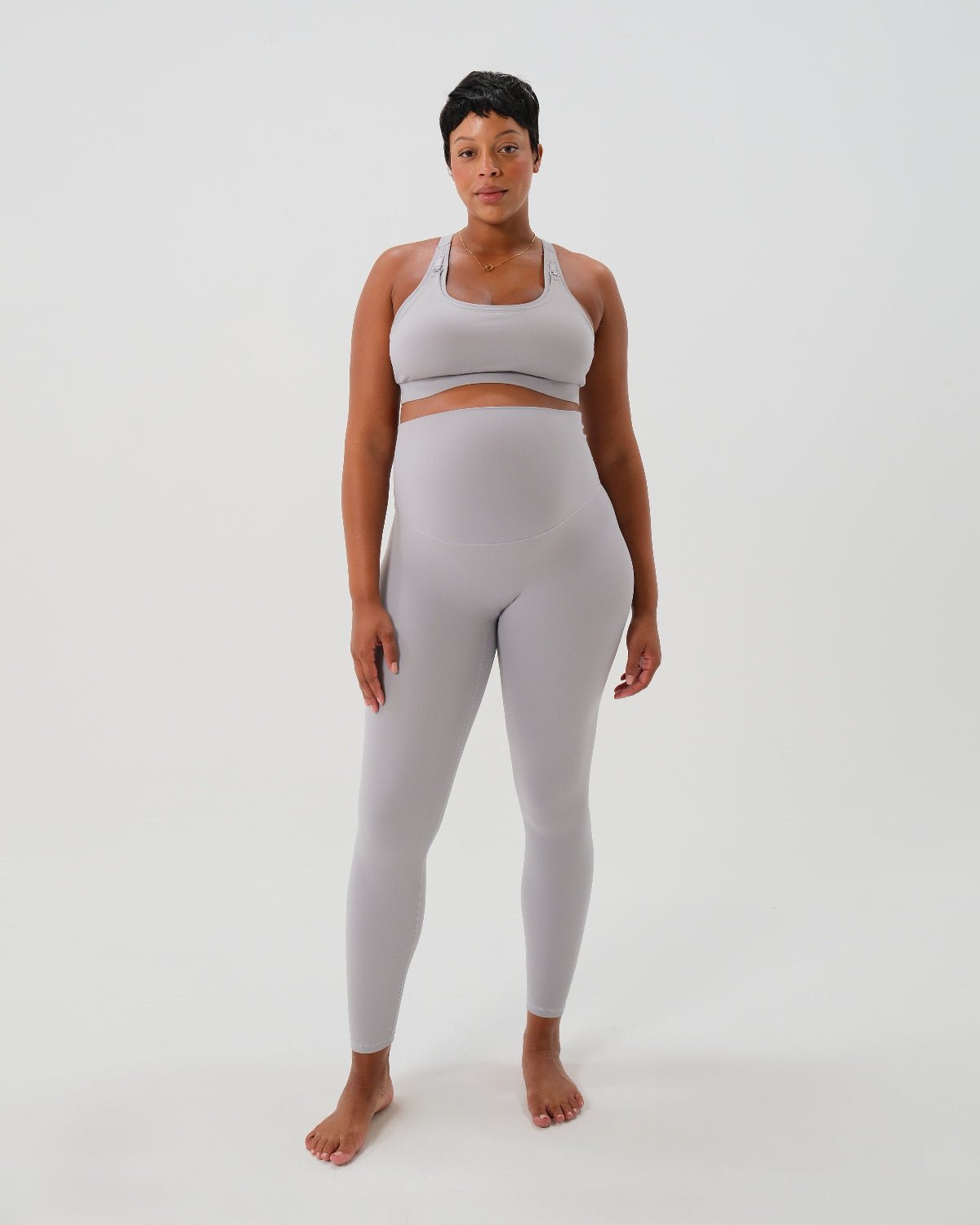 Pregnant woman wearing premium light grey maternity leggings with a flattering scrunch butt and supportive high waist and a high impact, racer back nursing sports bra on a white background. Premium maternity athletic and activewear by AXK - petite, tall and plus size friendly. 