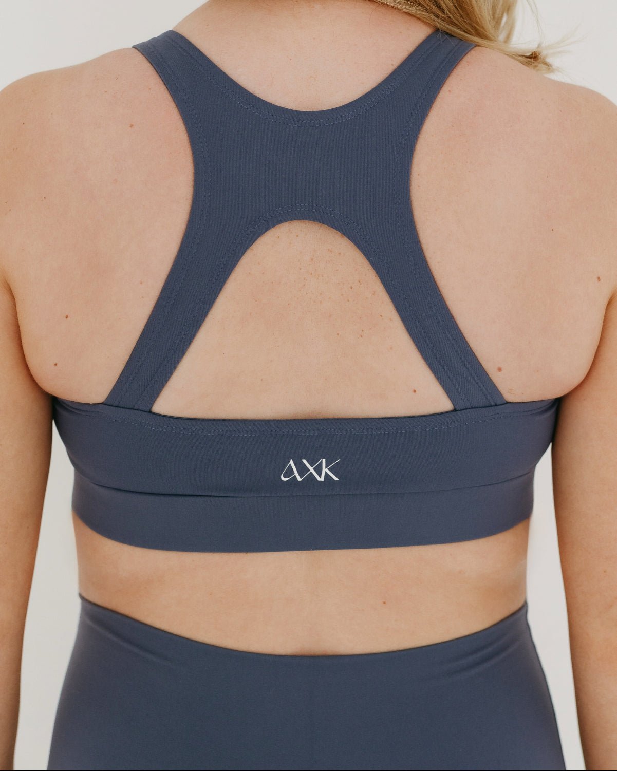 Pregnant woman wearing a blue maternity and nursing sports bra and pregnancy leggings on a plain background.