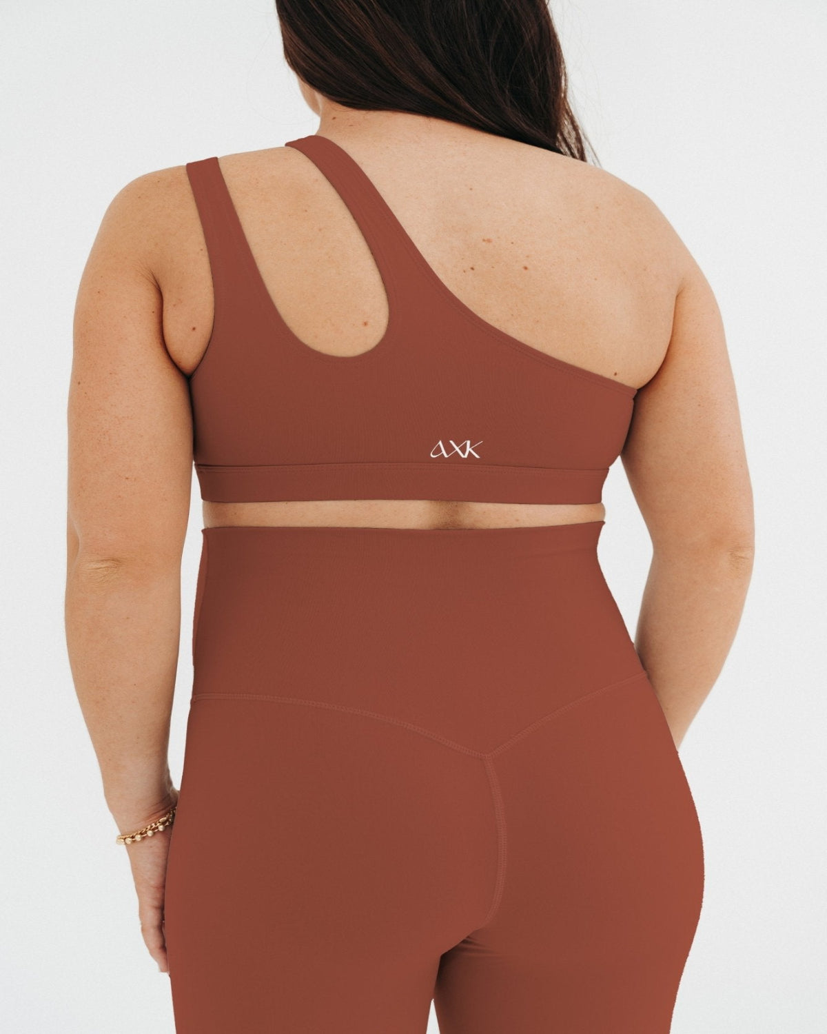 Pregnant woman wearing premium brown AXK maternity leggings with a supportive high waist and matching high-impact racerback maternity and nursing sports bra, standing against a white background. Premium maternity athletic and activewear by AXK - high quality petite, tall, and plus size maternity. 