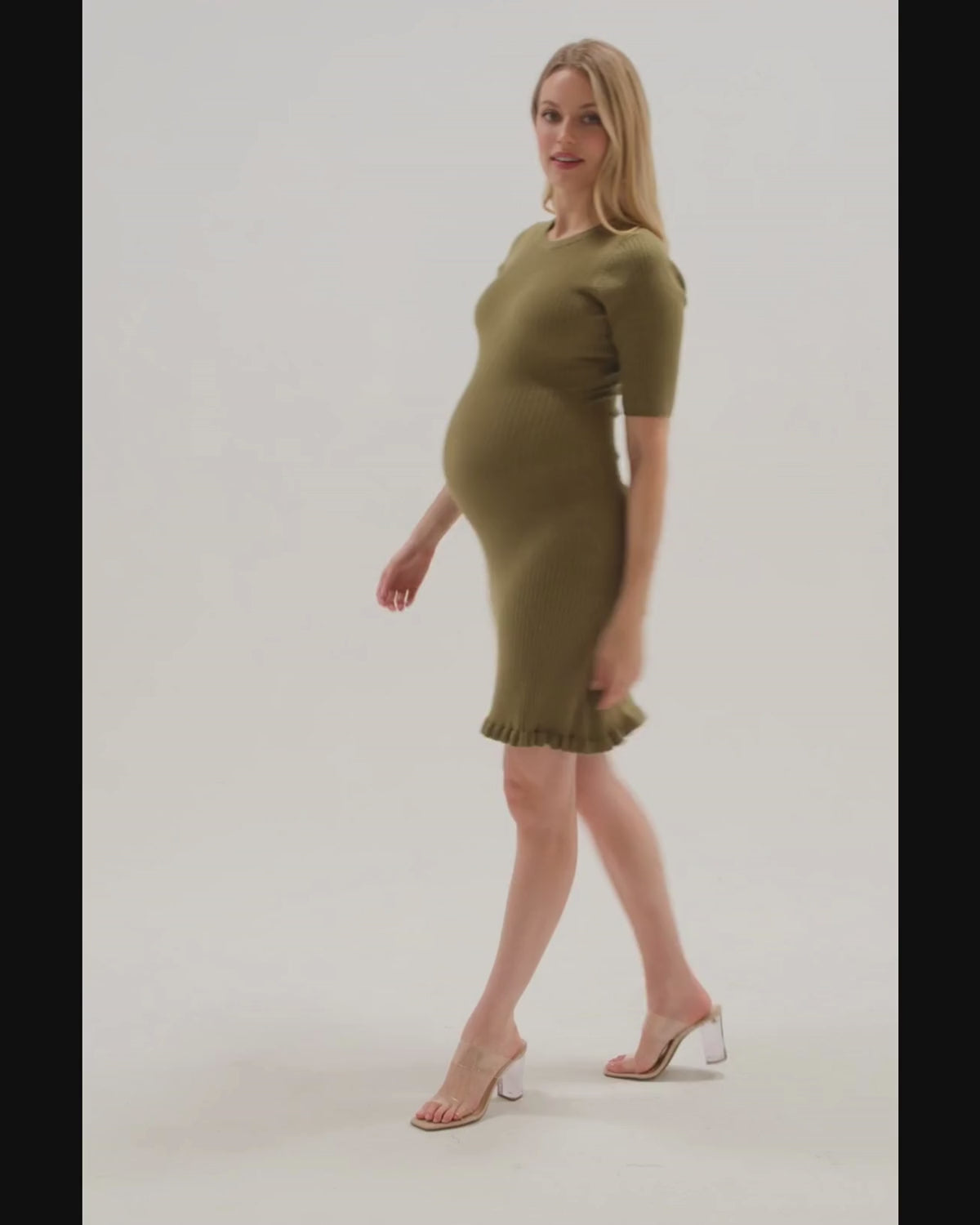 Video of a pregnant woman wearing a premium olive green maternity sweater dress with 3/4 sleeves, feminine ruffle hem detail, and luxurious cotton stretch knit. This best in class design is perfect for work outfits, wedding guest, holiday parties, baby showers, and street style. Postpartum friendly. 2026 MARION core season collection. 