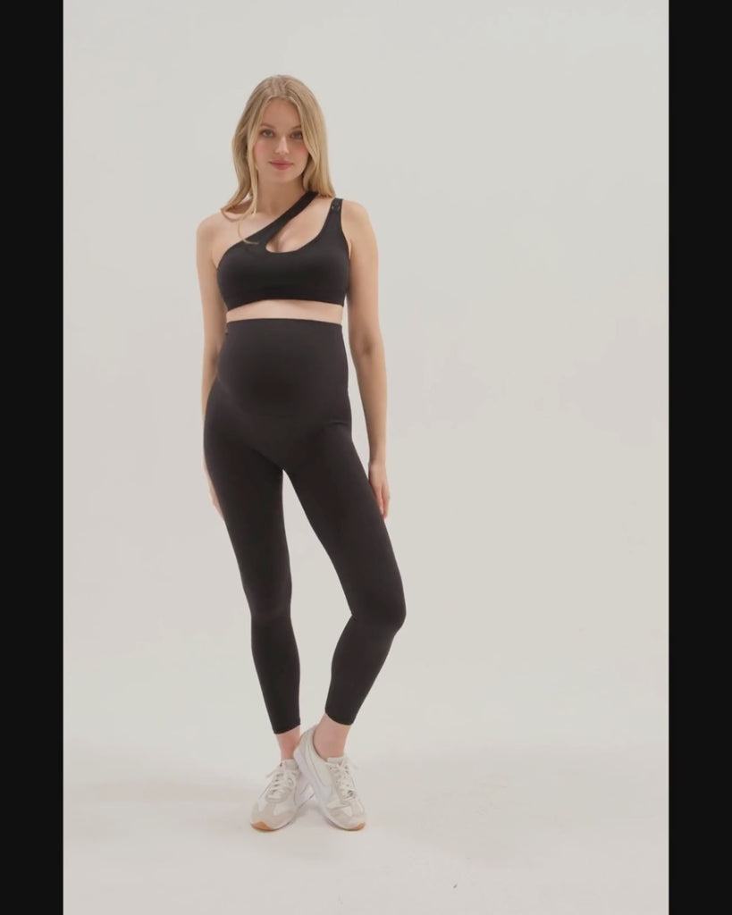 Pregnant model wearing premium black AXK maternity leggings with a supportive high waist, bum flattering back v seam, seamless front design, and butter soft stretch fabric. Best selling with glowing 5-star reviews, these leggings are perfect for running, pregnancy yoga, walking, biking, or loungewear. High quality 2026 maternity athletic and activewear in regular and plus sizes. Petite and tall friendly. 