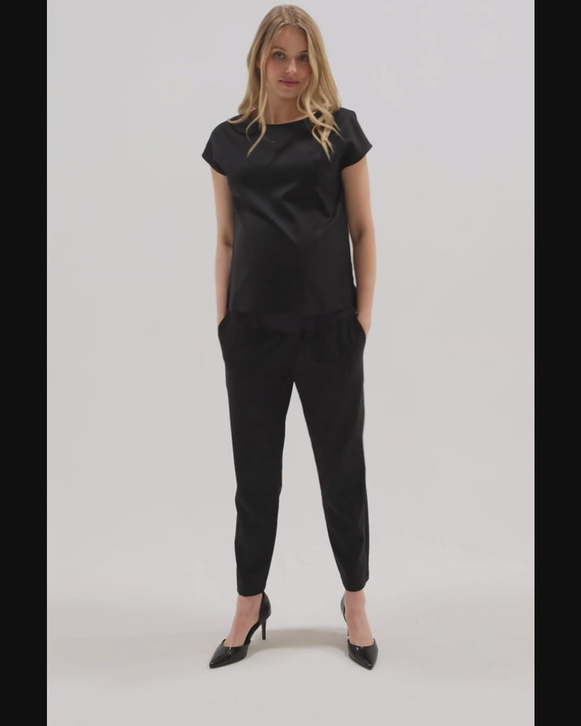 Video showing pregnant woman wearing black MARION maternity dress pants, under belly style, cut in all-season wool blend with hidden flexible waist adjustment, deep pockets, and stylish straight leg. Maternity trousers cropped for tall mamas and full length for petite pregnant women. Postpartum friendly women's wear for business, wedding guest, dinner, and occasion. 